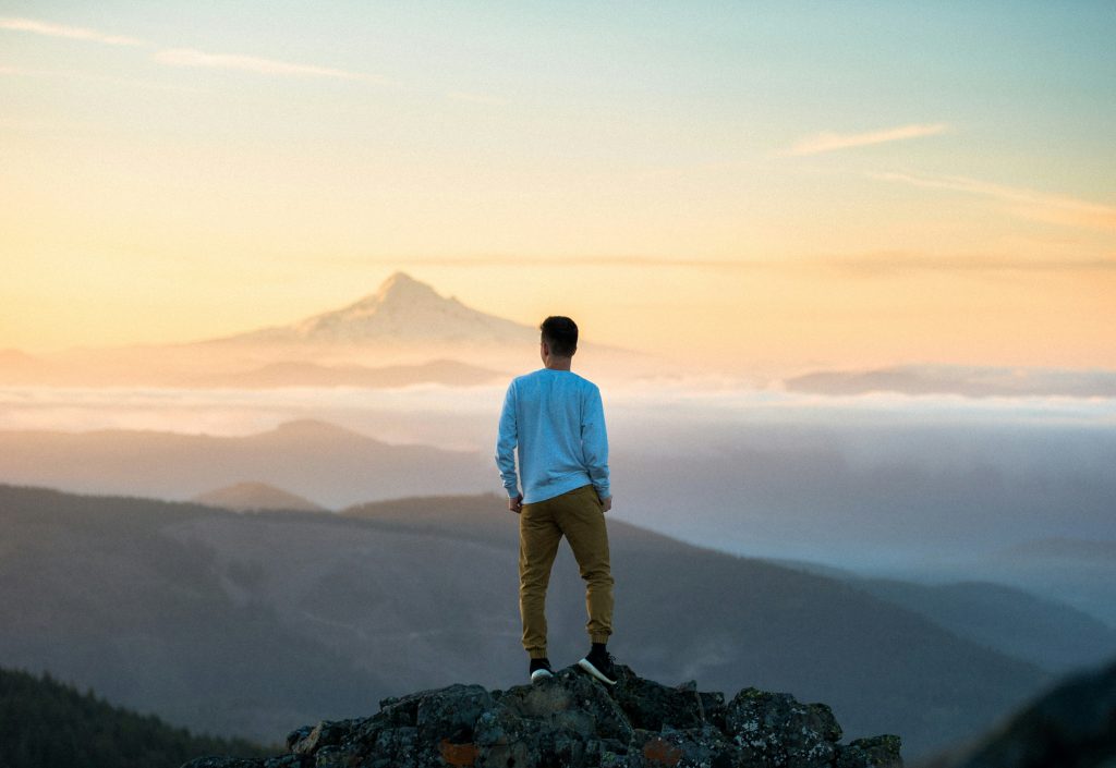 Man standing on a hill looking at a mountain horizon scene