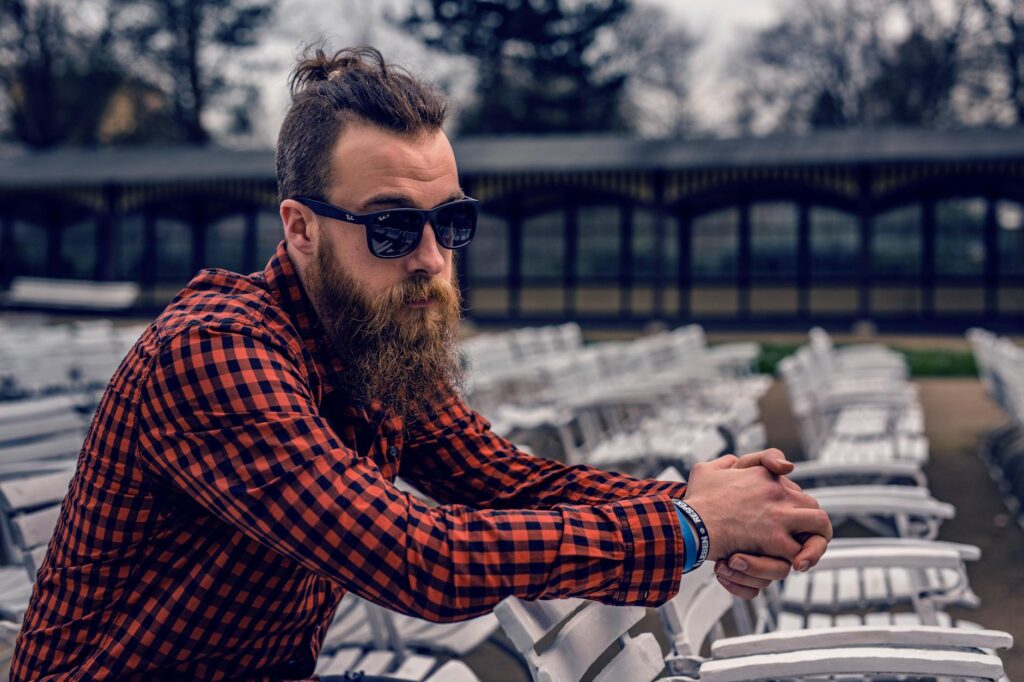 man wearing black and red checkered long sleeve shirt wearing black wayfarer sunglasses sitting on white wooden chair